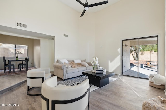 living area with a high ceiling, light wood-type flooring, and ceiling fan