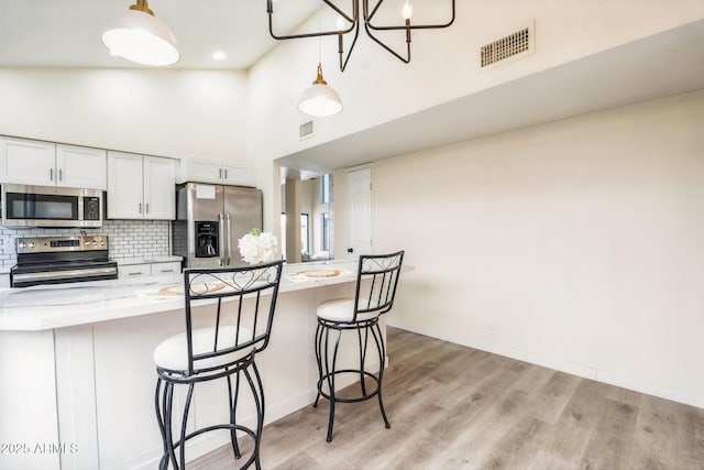 kitchen featuring stainless steel appliances, a breakfast bar, tasteful backsplash, a high ceiling, and white cabinetry