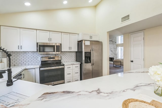 kitchen featuring appliances with stainless steel finishes, decorative backsplash, white cabinets, recessed lighting, and high vaulted ceiling