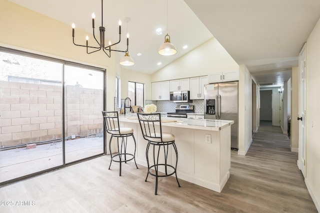kitchen featuring stainless steel appliances, light wood-type flooring, a kitchen bar, white cabinetry, and backsplash