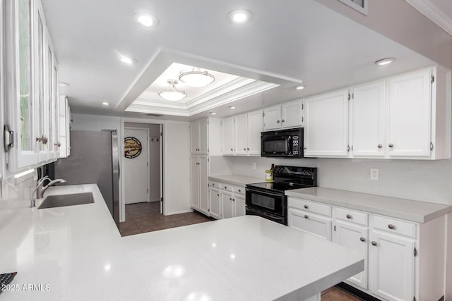 kitchen with a tray ceiling, white cabinetry, black appliances, and a sink