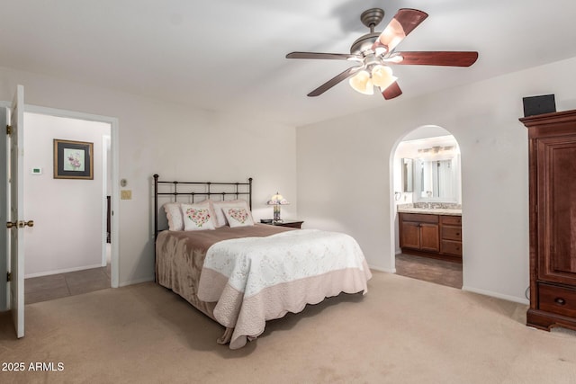 bedroom featuring light carpet, ensuite bath, arched walkways, and baseboards