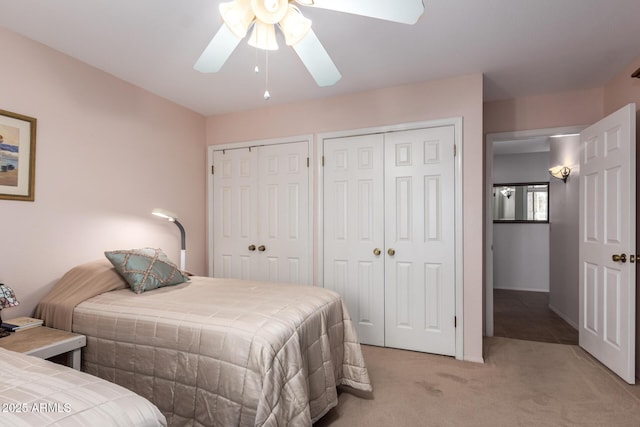 bedroom with a ceiling fan, two closets, and light carpet