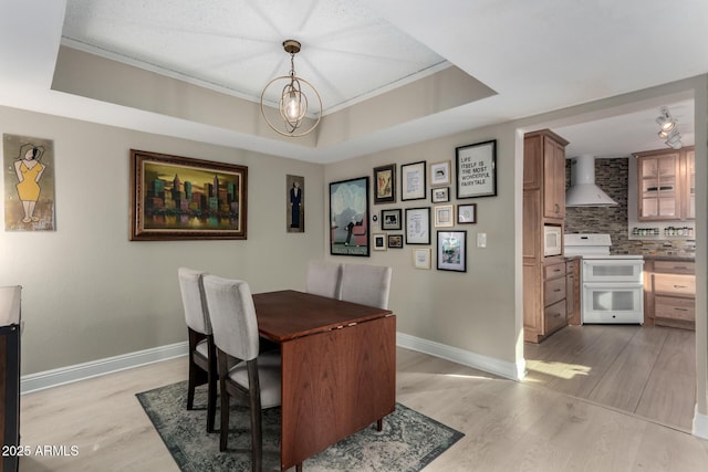 dining room with a raised ceiling, light hardwood / wood-style floors, and a notable chandelier