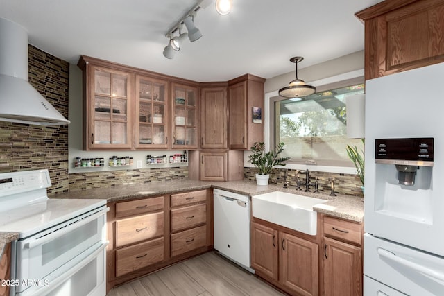 kitchen with sink, decorative light fixtures, white appliances, light stone countertops, and wall chimney range hood