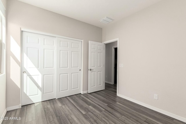 unfurnished bedroom featuring a closet, visible vents, dark wood-type flooring, and baseboards