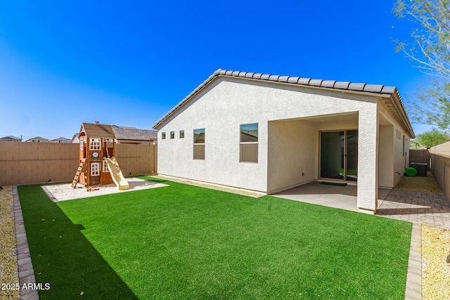 rear view of property featuring a playground, stucco siding, a lawn, a fenced backyard, and a patio area