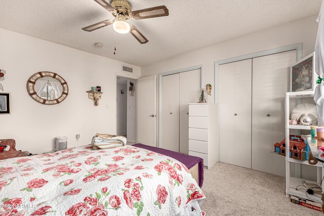 bedroom with ceiling fan, a textured ceiling, light carpet, and two closets