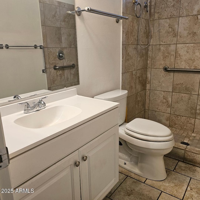 bathroom with toilet, a tile shower, and vanity