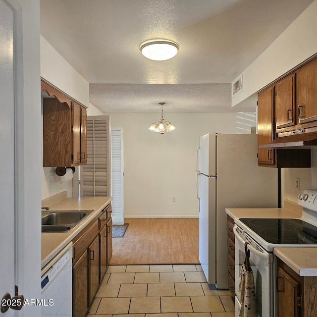 kitchen with white appliances, a textured ceiling, sink, pendant lighting, and a chandelier