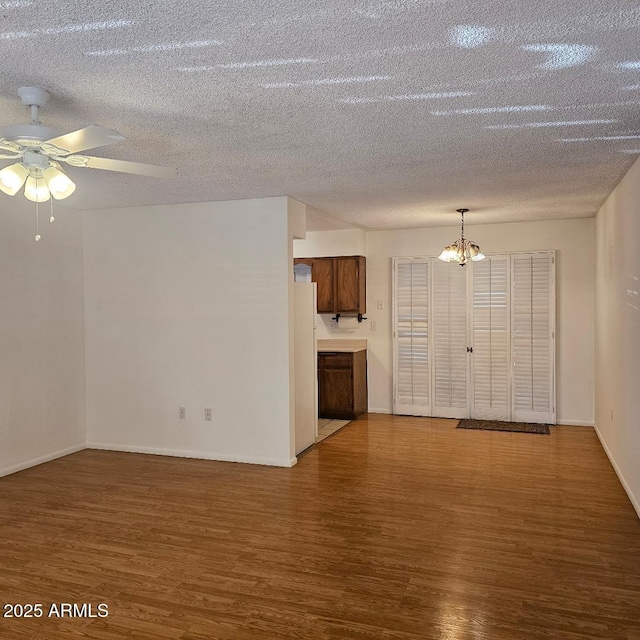 unfurnished living room featuring ceiling fan with notable chandelier, wood-type flooring, and a textured ceiling