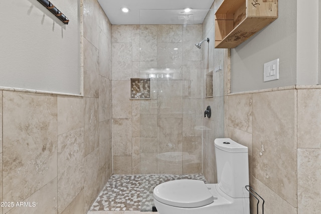 bathroom with tile walls, toilet, a tile shower, recessed lighting, and a wainscoted wall