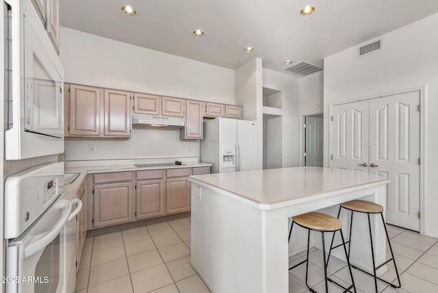 kitchen featuring a center island, white appliances, light countertops, under cabinet range hood, and visible vents
