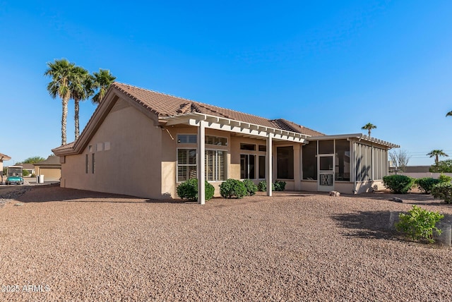 rear view of house featuring a tile roof, a sunroom, and stucco siding