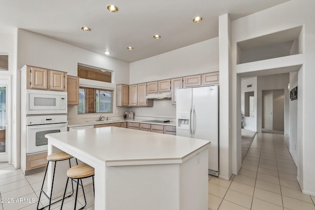 kitchen featuring light brown cabinetry, under cabinet range hood, a sink, light tile patterned floors, and white appliances