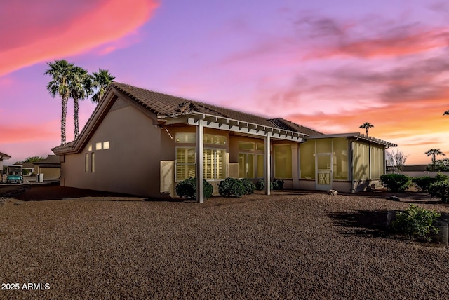 rear view of house featuring a pergola, stucco siding, a tile roof, a patio area, and a sunroom