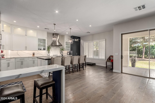 kitchen with wall chimney exhaust hood, a kitchen island, wood-type flooring, a kitchen bar, and white cabinets