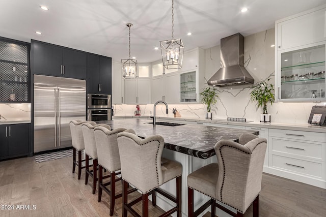 kitchen featuring wall chimney range hood, sink, dark hardwood / wood-style floors, an island with sink, and stainless steel appliances