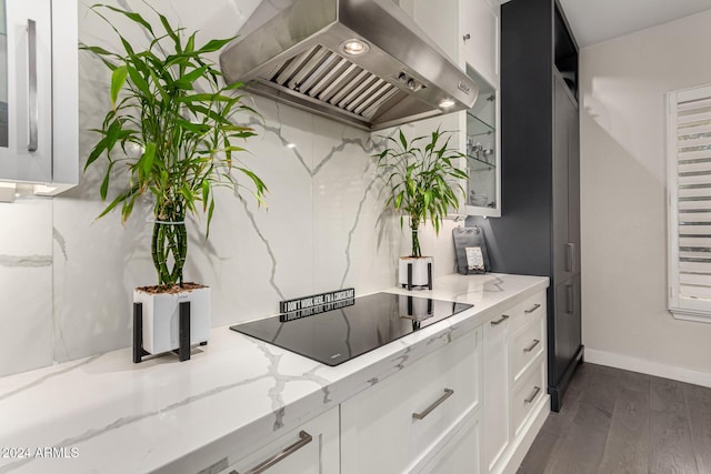 kitchen with black electric stovetop, light stone counters, white cabinetry, and range hood