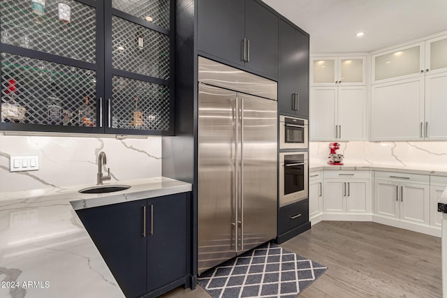 kitchen featuring light stone countertops, tasteful backsplash, stainless steel built in refrigerator, white cabinets, and light hardwood / wood-style floors