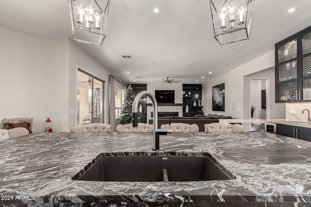 kitchen with stone counters, a tiled fireplace, ceiling fan, and sink