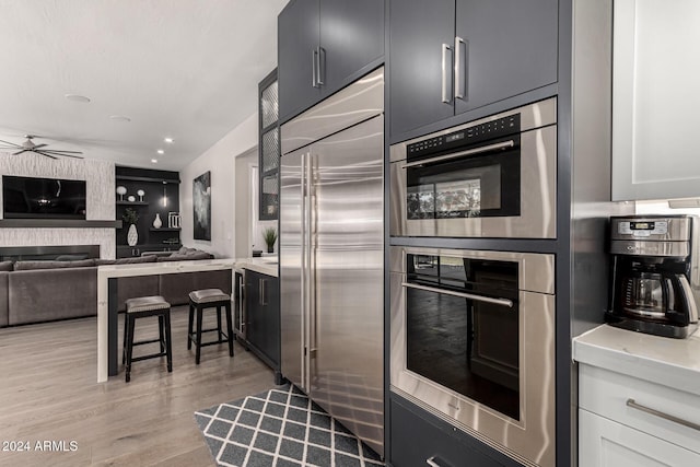 kitchen featuring ceiling fan, a large fireplace, light hardwood / wood-style floors, white cabinets, and appliances with stainless steel finishes