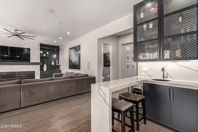 kitchen with ceiling fan, a large fireplace, sink, kitchen peninsula, and wood-type flooring