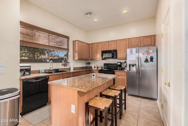 kitchen with sink, a breakfast bar, black appliances, light stone counters, and a center island