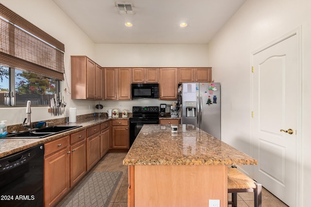 kitchen featuring a breakfast bar area, black appliances, light stone counters, and a center island