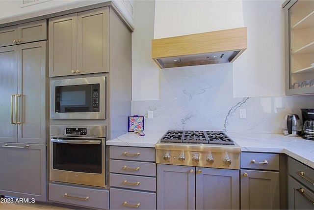 kitchen with built in appliances, light stone counters, tasteful backsplash, and range hood