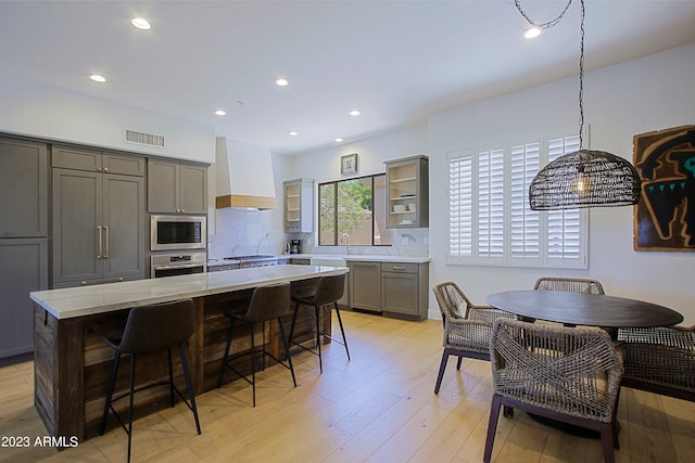 kitchen with light wood-type flooring, a center island, stainless steel appliances, gray cabinets, and custom range hood