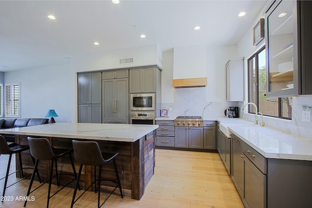 kitchen featuring tasteful backsplash, appliances with stainless steel finishes, sink, light wood-type flooring, and a kitchen bar