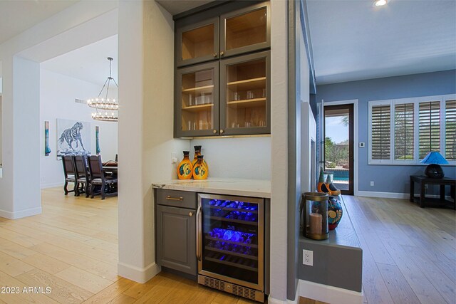 bar with hanging light fixtures, dark brown cabinetry, light hardwood / wood-style floors, and beverage cooler