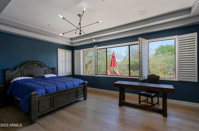 bedroom with a notable chandelier, light wood-type flooring, and a raised ceiling