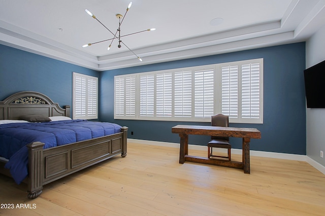 bedroom featuring a chandelier, multiple windows, light wood-type flooring, and a raised ceiling