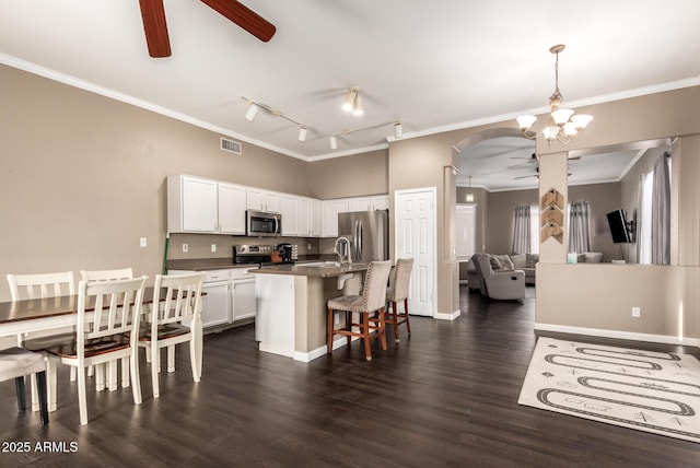 kitchen with appliances with stainless steel finishes, white cabinetry, hanging light fixtures, ornamental molding, and an island with sink