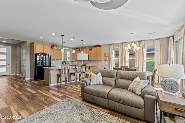 living area featuring dark wood-type flooring, an inviting chandelier, visible vents, and a healthy amount of sunlight