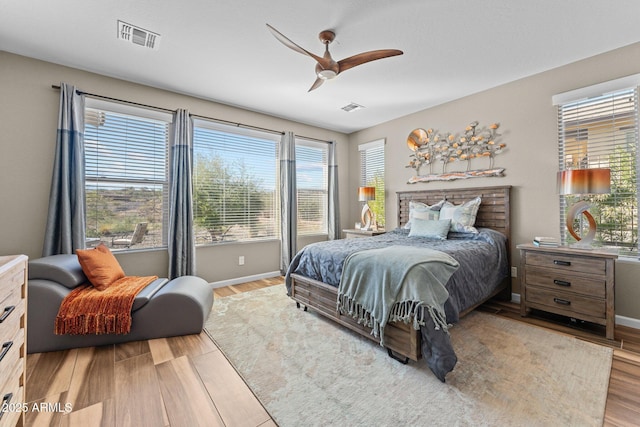 bedroom featuring a ceiling fan, wood finished floors, visible vents, and baseboards