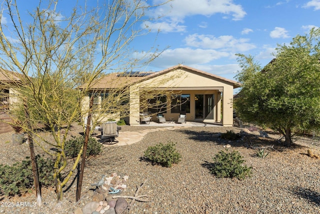 back of property with a patio area, roof mounted solar panels, and stucco siding