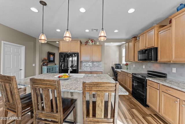 kitchen with a kitchen island with sink, wood finished floors, visible vents, backsplash, and black appliances