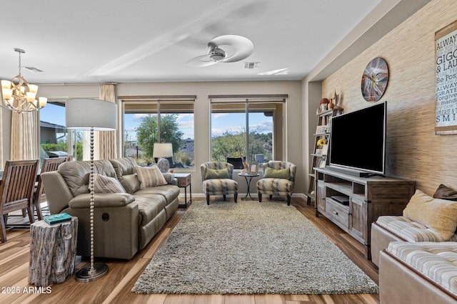 living room featuring an accent wall, ceiling fan with notable chandelier, visible vents, and wood finished floors