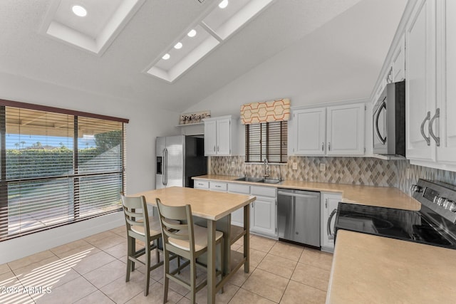 kitchen with sink, light tile patterned floors, vaulted ceiling with skylight, white cabinetry, and appliances with stainless steel finishes