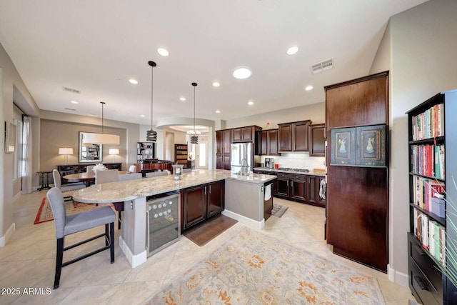 kitchen with dark brown cabinets, beverage cooler, freestanding refrigerator, a large island, and visible vents