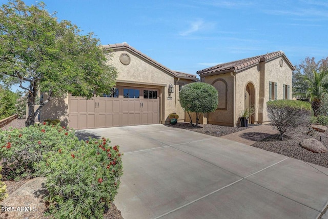 mediterranean / spanish home with an attached garage, driveway, a tile roof, and stucco siding