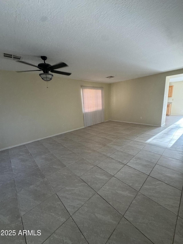 tiled empty room with baseboards, a textured ceiling, visible vents, and ceiling fan