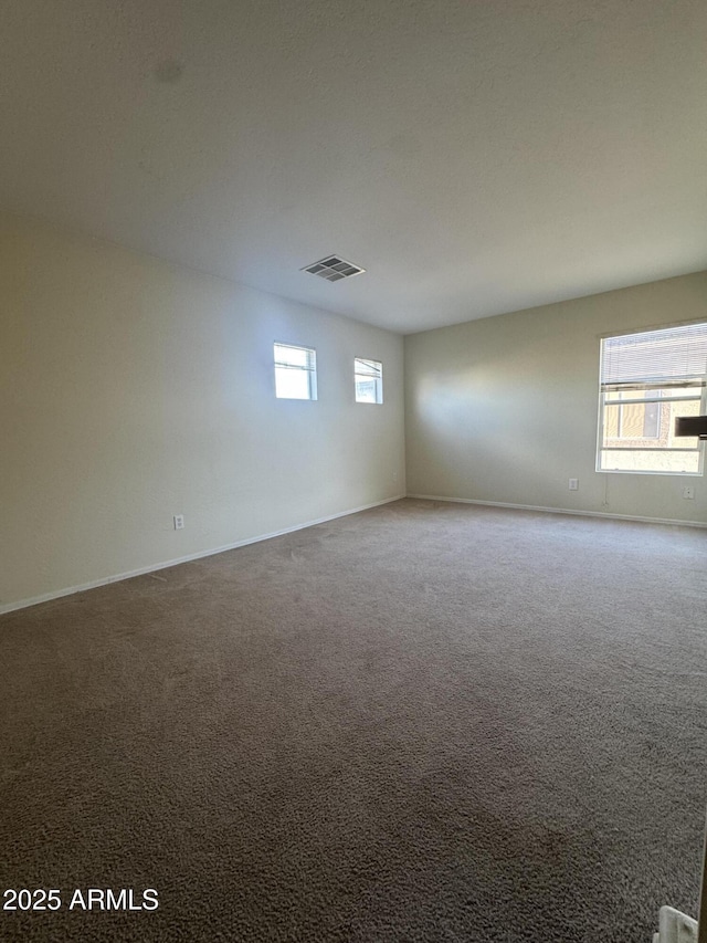 empty room featuring plenty of natural light, baseboards, carpet floors, and visible vents