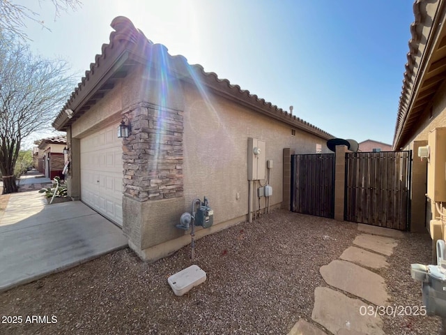 view of home's exterior featuring stucco siding, concrete driveway, a gate, and a garage
