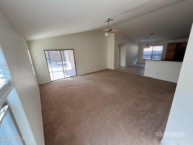 unfurnished living room featuring arched walkways, vaulted ceiling, a ceiling fan, and light carpet