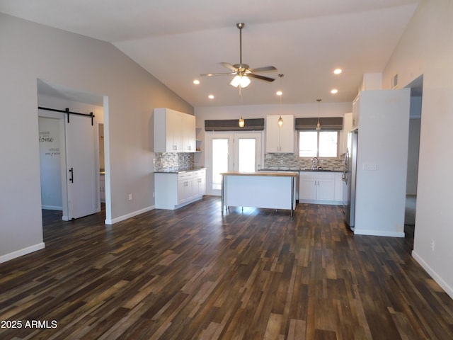 kitchen featuring vaulted ceiling, white cabinetry, sink, stainless steel fridge, and a barn door