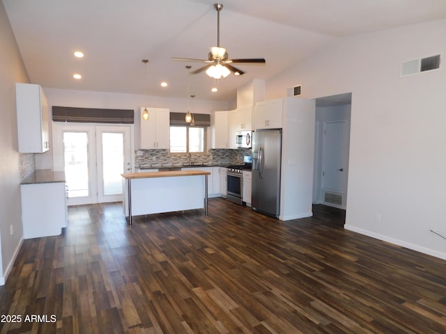 kitchen with dark wood-type flooring, lofted ceiling, appliances with stainless steel finishes, decorative backsplash, and white cabinets